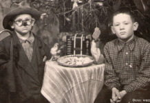 Weihnachten: Was die Exponate des Museums erzählen 1.1.87 Kinder am Weihnachtsbaum. Einer der Jungen in Verkleidung. Auf dem Tisch ein Teller mit Keksen, zwei Zelluloidhähne, Spielzeugakkordeon. 1950er Jahre, Gebiet Karaganda. Lissakowsk-Museum.