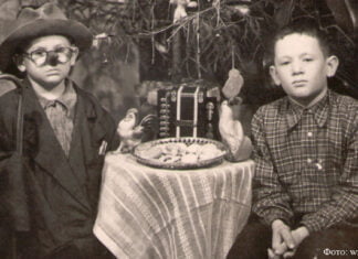 Weihnachten: Was die Exponate des Museums erzählen 1.1.87 Kinder am Weihnachtsbaum. Einer der Jungen in Verkleidung. Auf dem Tisch ein Teller mit Keksen, zwei Zelluloidhähne, Spielzeugakkordeon. 1950er Jahre, Gebiet Karaganda. Lissakowsk-Museum.