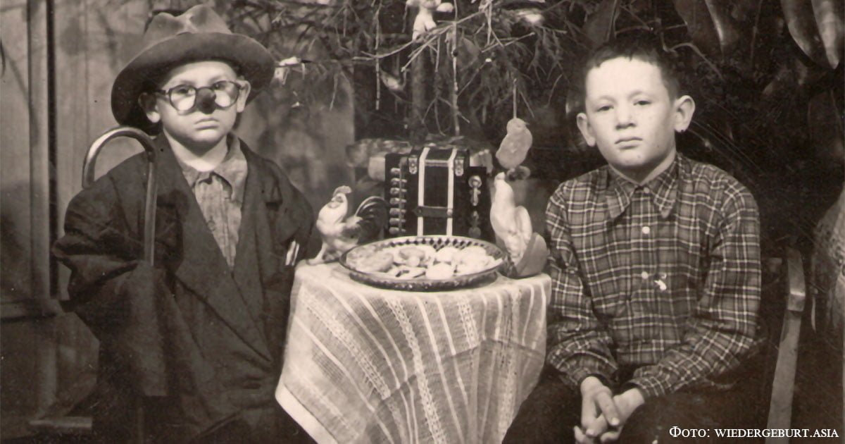1.1.87 Kinder am Weihnachtsbaum. Einer der Jungen in Verkleidung. Auf dem Tisch ein Teller mit Keksen, zwei Zelluloidhähne, Spielzeugakkordeon. 1950er Jahre, Gebiet Karaganda. Lissakowsk-Museum.